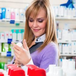 Portrait einer blonden Frau die sich Produkte in der Apotheke ansieht.