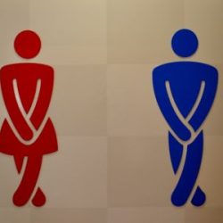 Toilettenzeichen, rot Frau, blau Mann, beide mit verschränkten Beinen