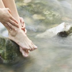 Eine Frau taucht ihre Füße in einen Waldbachlauf.