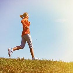 Eien Frau joggt an einem Hang vor blauem Himmel.