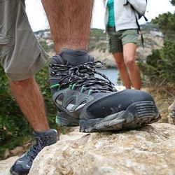 Ein Wanderer stützt einen Fuß auf den Stein, im Hintergrund eine Wanderin.