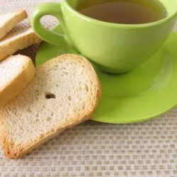 Tee in grüner Tasse mit Zwieback am Rand.