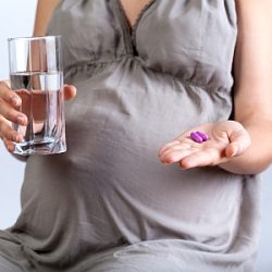 Eine schwangere Frau mit einem Glas Wasser und Medizin in der Hand.